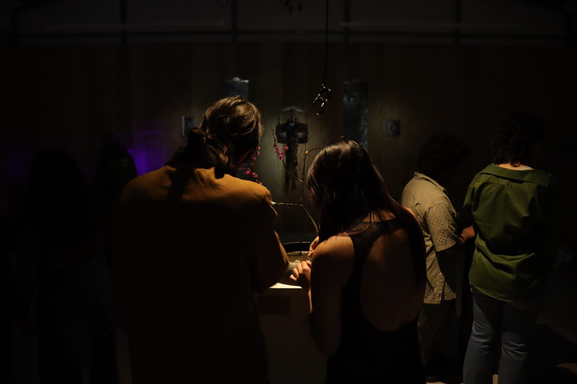 Visitors gathered closely around a work in the dim gallery.