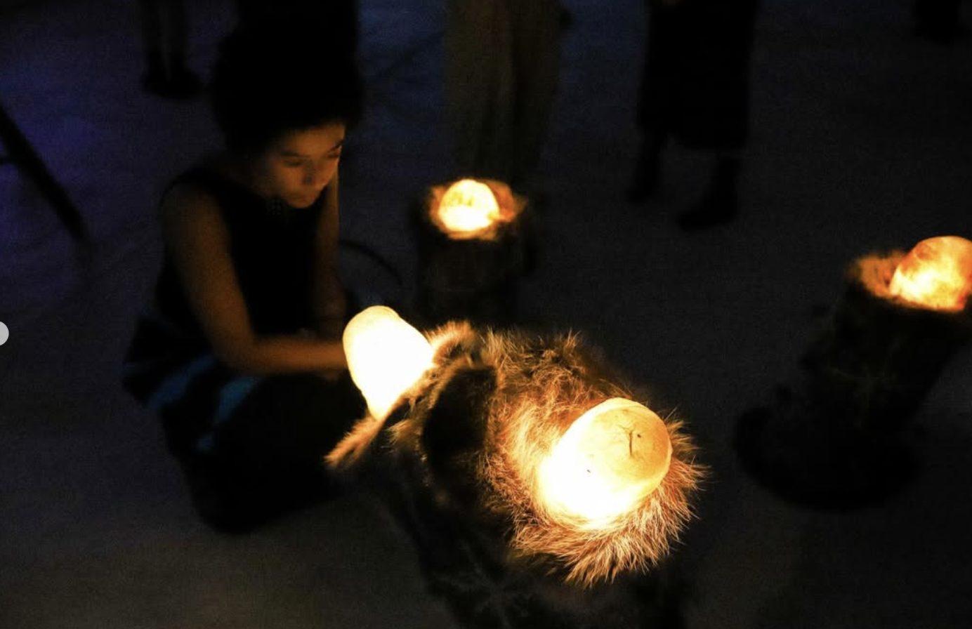 A visitor kneels beside glowing, fibrous orb-like lamps on the floor.